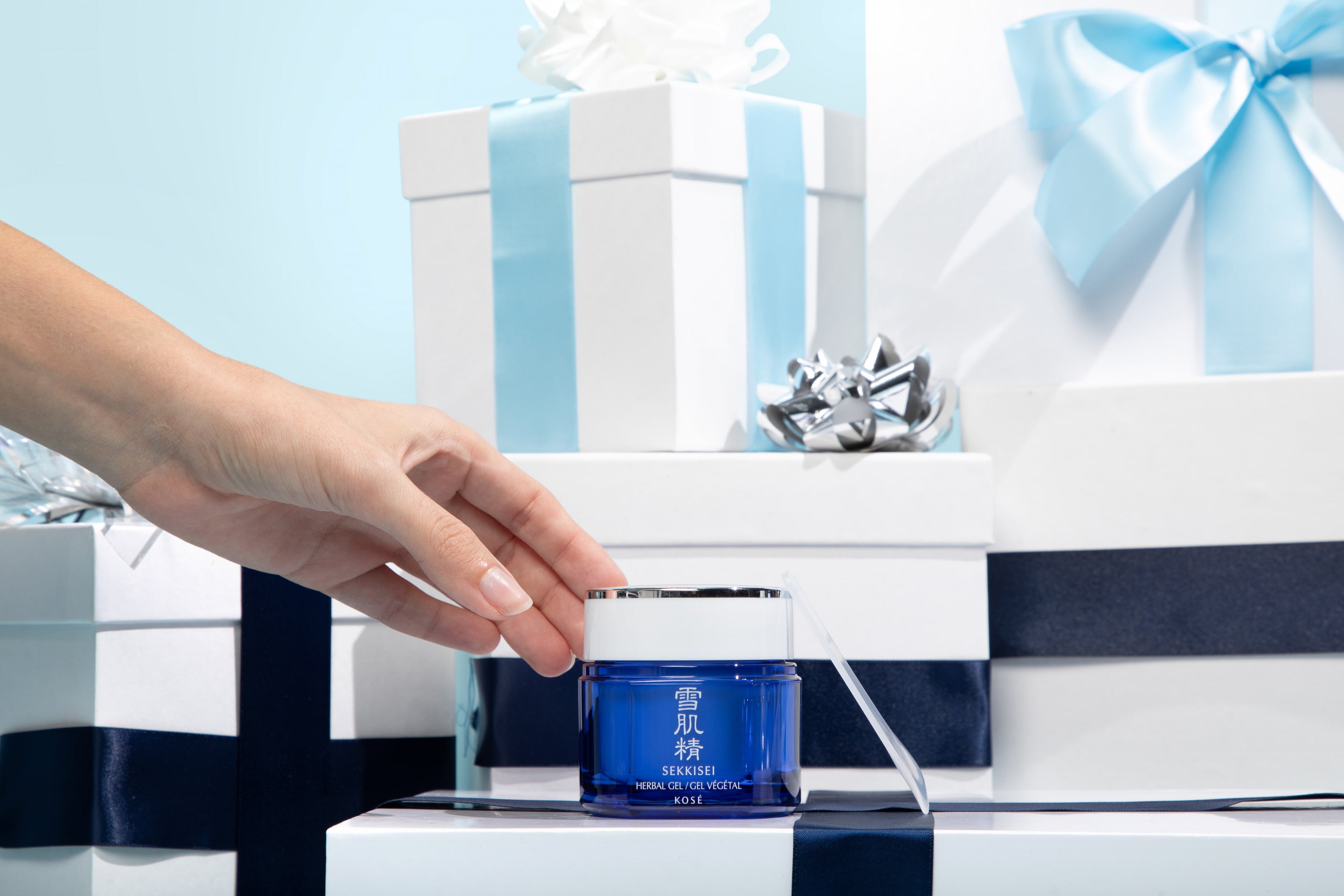Hand reaching for SEKKISEI Herbal Gel on top of gift boxes